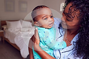 Loving African American Mother Wearing Pyjamas Cuddling Baby Daughter In Bedroom At Home