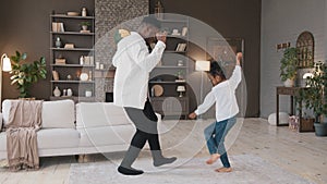 Loving african dad dancing with cute child daughter in living room happy father and small kid girl playing jumping