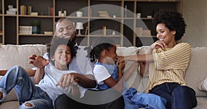 Loving Afro American family couple with children tickle on couch