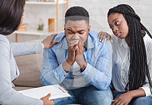 Loving afro wife and unrecognizable psychotherapist supporting guy during therapy session