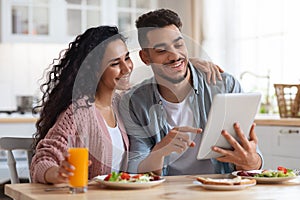 Loving Arab Couple Eating Breakfast Together And Using Digital Tablet In Kitchen