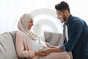 Loving Arab Husband Placing Wireless Headphones On Pregnant Wife& x27;s Belly