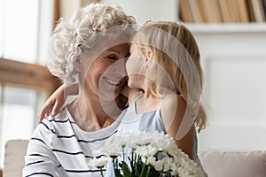 Loving attentive little granddaughter congratulating happy mature granny with birthday