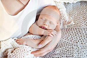 Loving baby sleeping in mother`s hands. Closeup picture. Happy mother and her slipping newborn baby in the bed