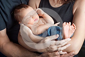 Loving baby sleeping in parents hands. Closeup picture. Happy mother and father and they slipping newborn baby