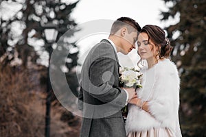 Loving and beautiful bride and groom stand in an embrace in the winter forest