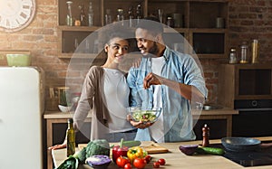 Loving black couple cooking green salad in kitchen