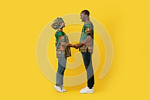 Loving black couple in national costumes bonding on yellow