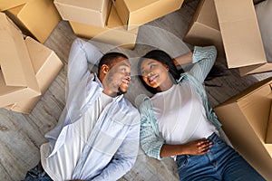 Loving black family with carton boxes around, lying on floor and having rest on moving day, top view