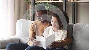 Loving black father embrace kid daughter reading book at home