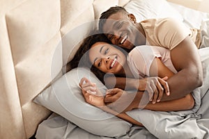 Loving black man hugs wife lying in bed in morning
