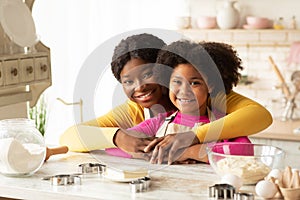 Loving Black Mom And Daughter In Aprons Posing At Table In Kitchen