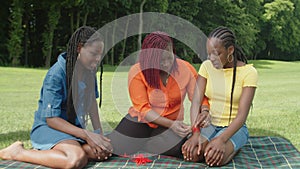 Loving black mother tying red thread around daughters wrist outdoors