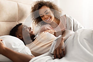 Loving black spouses flirting lying in bed enjoying romantic morning