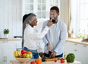 Loving black woman feeding her husband while they cooking together at kitchen