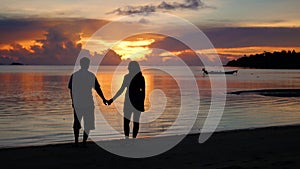 Loving boy and girl walking on the beach at sunset time. Silhouettes