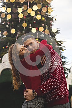 Loving boyfriend and girlfriend are hugging by Christmas tree