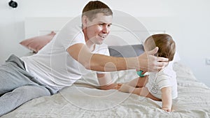 Loving caring father is playing with his little child and stroking his head in bedroom in holidays