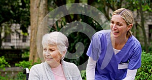 Loving, caring nurse assisting a disabled senior lady in a wheelchair outside in a garden at retirement home. Smiling