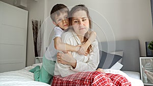 Loving and caring son comforting and hugging his mother sitting on bed. Concept of loving family, parents and kids, love and