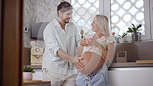 Loving Caucasian couple at home in kitchen feeling baby kick together. Pregnant mom and Smiling dad