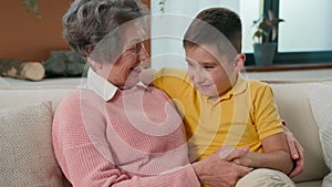 Loving Caucasian grandmother elderly woman fun spend weekend with grandson kid boy child at home on cozy sofa smiling