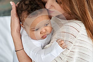 Loving caucasian mother hugging cute infant african american baby daughter.