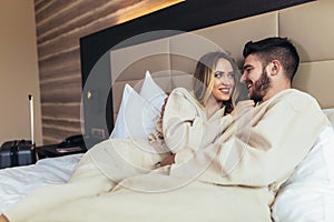 Loving couple in bathrobes relaxing on bed at hotel