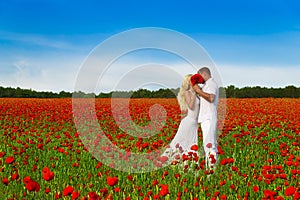 Loving couple with big flowers bouquet in white cloth kiss and hug in beautiful poppy field during romantic date.