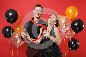 Loving couple in black clothes hold heart celebrating birthday holiday party on bright red background air