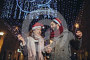 Loving couple burning sparklers by holiday illumination on new years eve