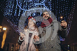 Loving couple burning sparklers by holiday illumination on new years eve