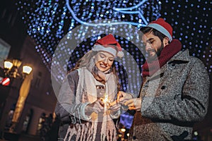 Loving couple burning sparklers by holiday illumination on new years eve