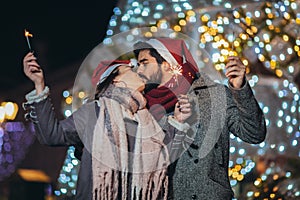 Loving couple burning sparklers by holiday illumination on new years eve