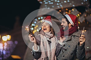 Loving couple burning sparklers by holiday illumination on new years eve