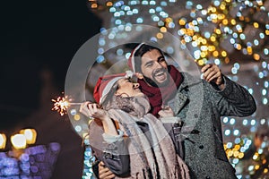 Loving couple burning sparklers by holiday illumination on new years eve