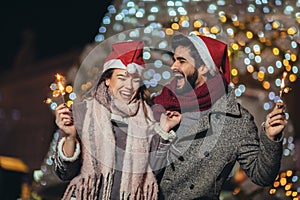 Loving couple burning sparklers by holiday illumination on new years eve