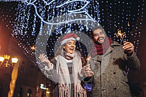 Loving couple burning sparklers by holiday illumination on new years eve