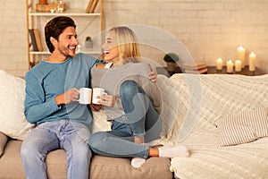 Loving Couple Clanging Cups Together Sitting On Couch At Home