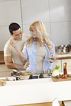 Loving couple cooking and tasting food in kitchen