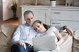 Loving couple cuddle on couch watching video on laptop