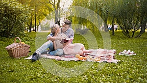 Loving couple discussing book, sitting on rug during picnic, romantic date