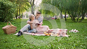 Loving couple discussing book snugly sitting on rug during picnic, romantic date