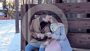 Loving couple drinking hot tea in backyard of cottage in winter
