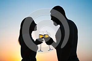 Loving couple drinking wine or champagne during sunset time, silhouette of a couple with wineglasses on sunset background, man and