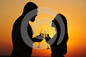loving couple drinking wine or champagne during sunset time, silhouette of a couple with wineglasses on sunset background, man