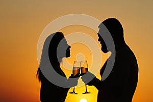 Loving couple drinking wine or champagne during sunset time, silhouette of a couple with wineglasses on sunset background, man and
