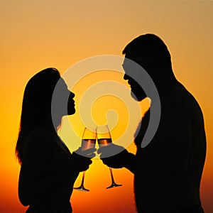 Loving couple drinking wine or champagne during sunset time, silhouette of a couple with wineglasses on sunset background, man and