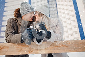 Loving couple drinks hot tea or coffee from thermos mugs on winter street in ice rink