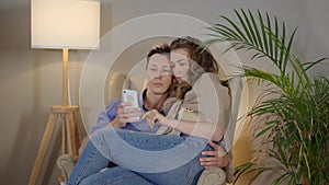 Loving couple embracing on armchair. Happy freelancers with laptop